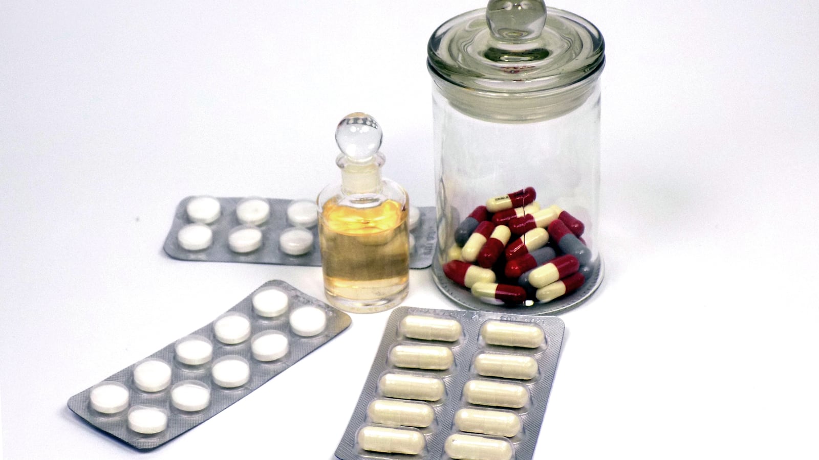 Tablets in strips beside a glass jar of capsules