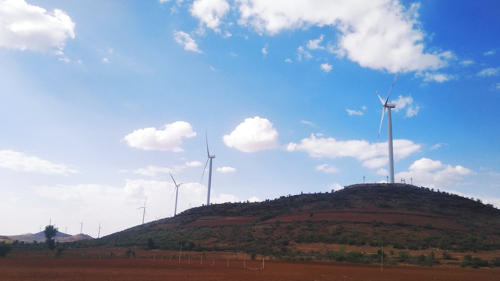 Wind turbines on a red earth hill under a blue sky in India